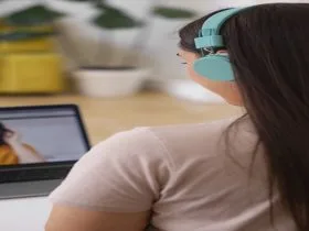 Pessoa em momento de concentração, usando fones coloridos enquanto interage por videochamada no notebook